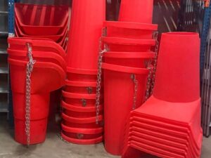 Stacked red plastic rubbish chute hoppers and straight sections in warehouse, featuring top entry funnels, tapered 20" sections with galvanised chains and brackets for secure connection – ideal for safe debris disposal from scaffolding on construction sites