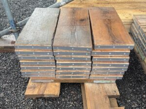 Pile of short 2ft (60cm) used scaffold planks, rustic brown wood with protective steel straps, second-hand construction timber