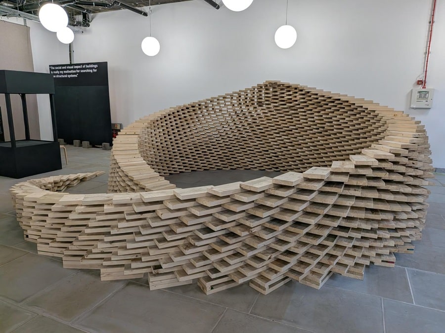 Curved exhibition sculpture constructed from layered sections of used scaffold boards
